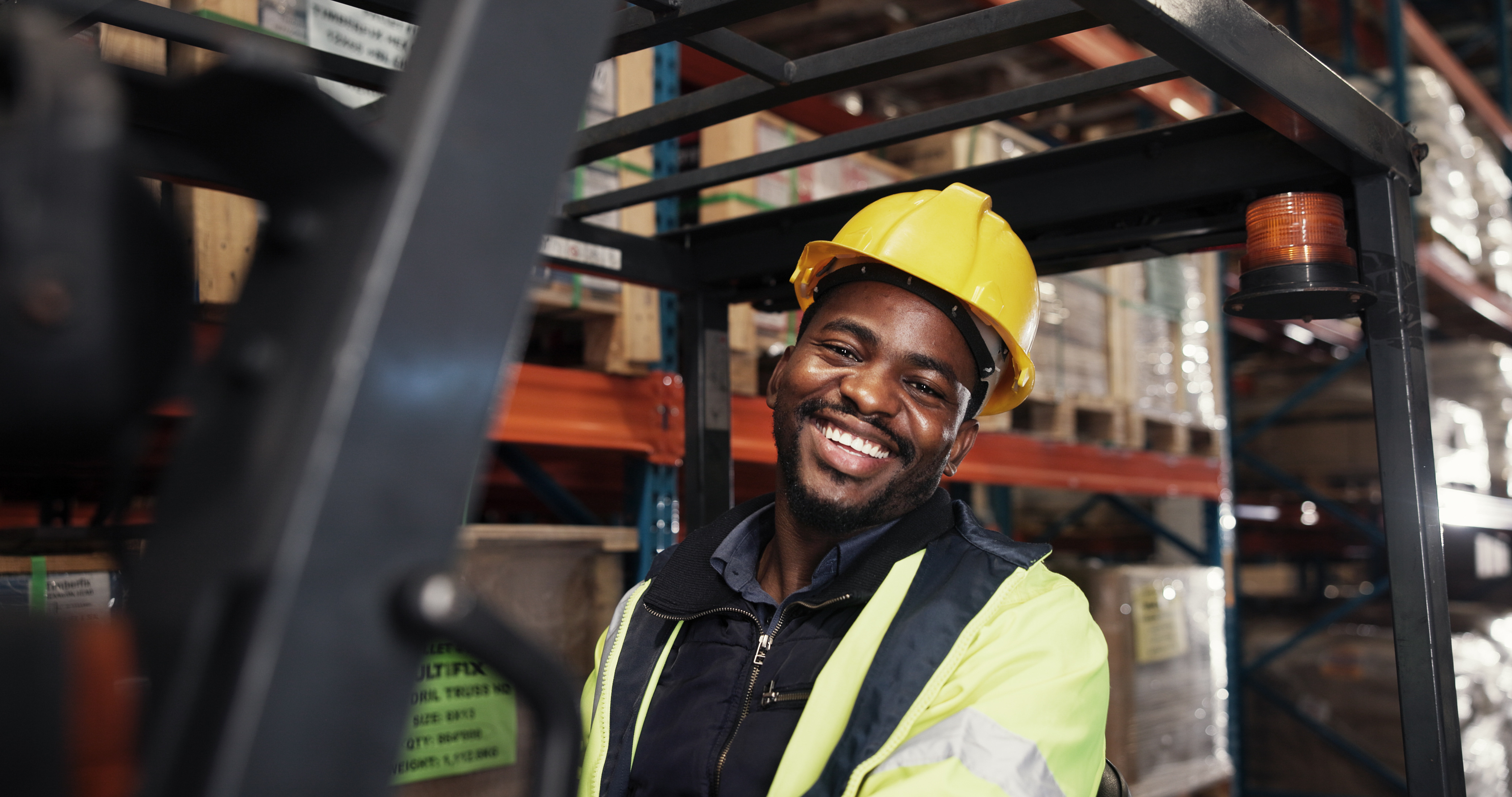 Smiling warehouse worker in yellow hard hat and safety vest in logistics facility